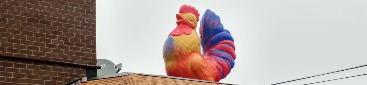 A colorful rooster statute approximately ten feet high, perched on the roof of the York Street Grille.