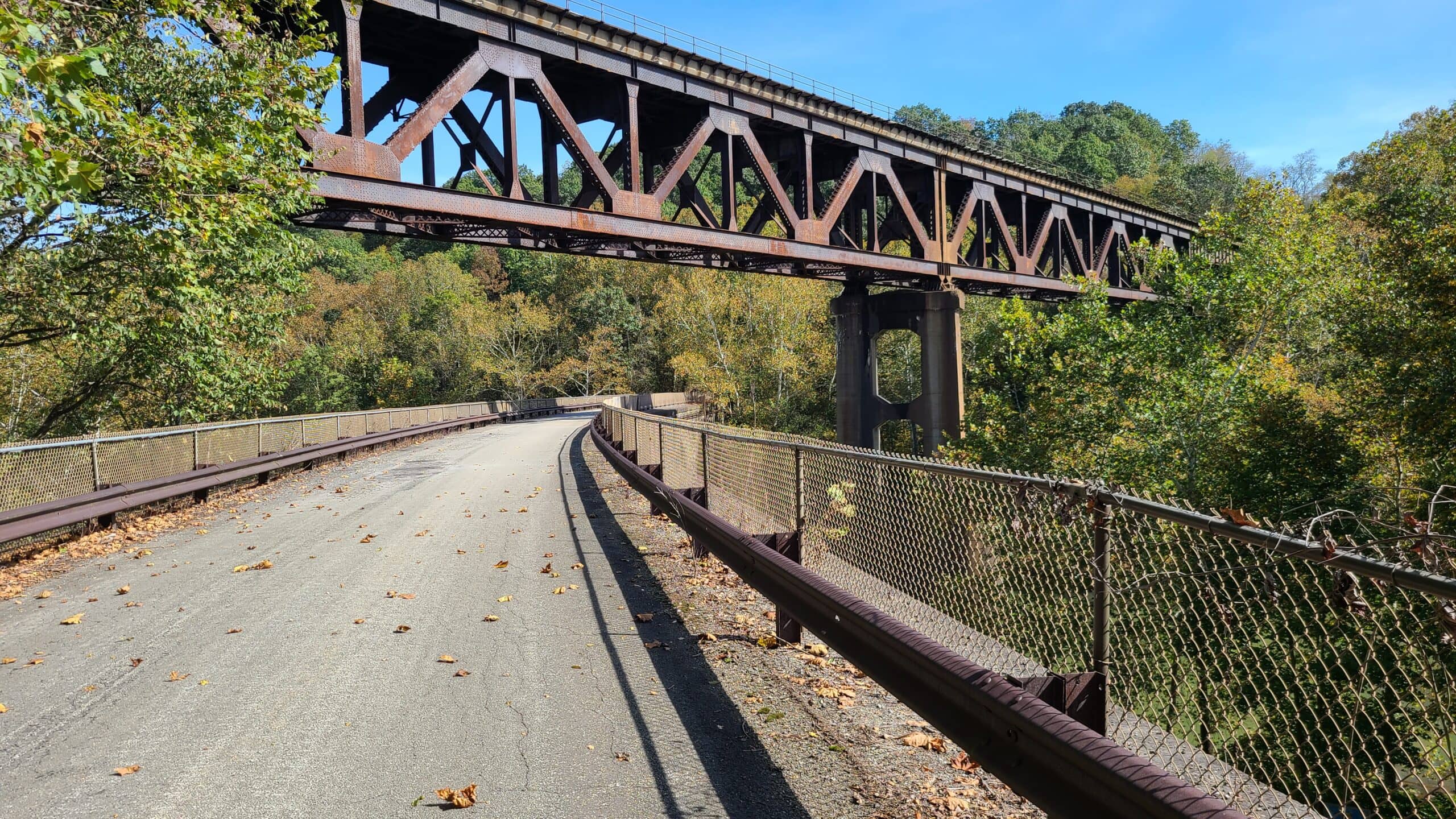 A metal truss railroad bridge runs above a stone railroad bridge.